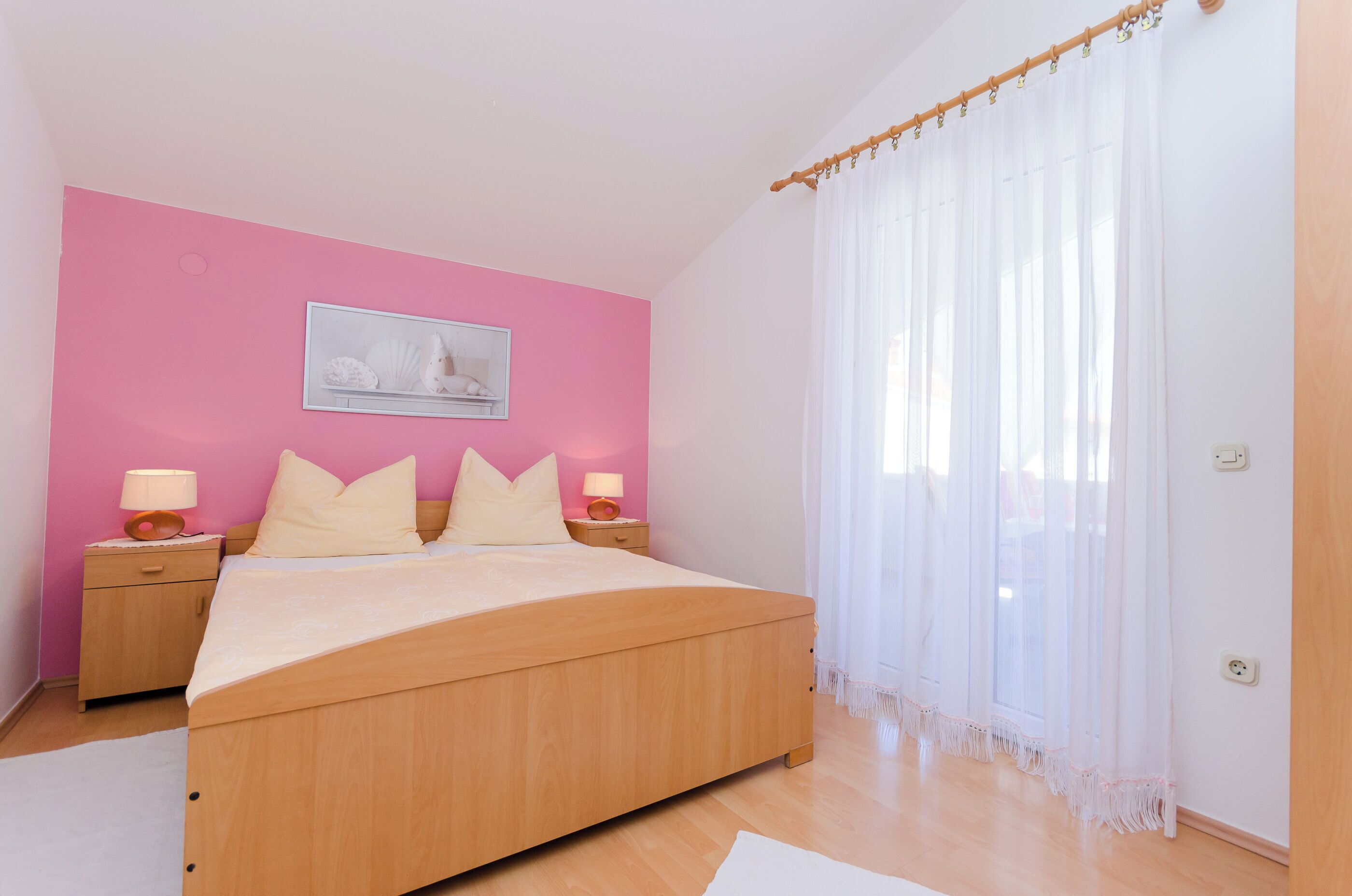 Een slaapkamer met een houten bed, roze wanden en witte gordijnen.