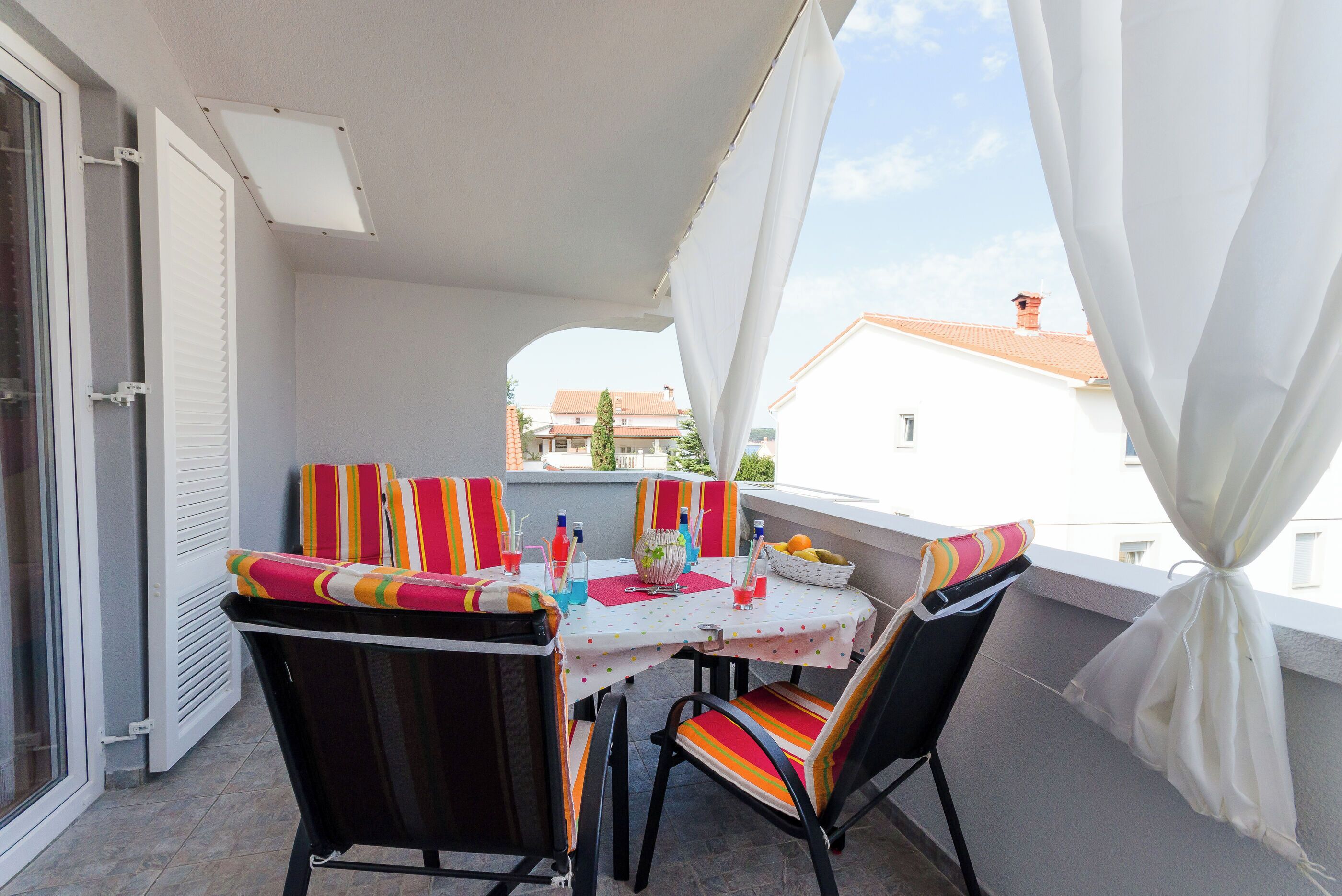 Ein Balkon mit Tisch für zwei Personen, Stühlen und Blick auf Gebäude im Hintergrund.