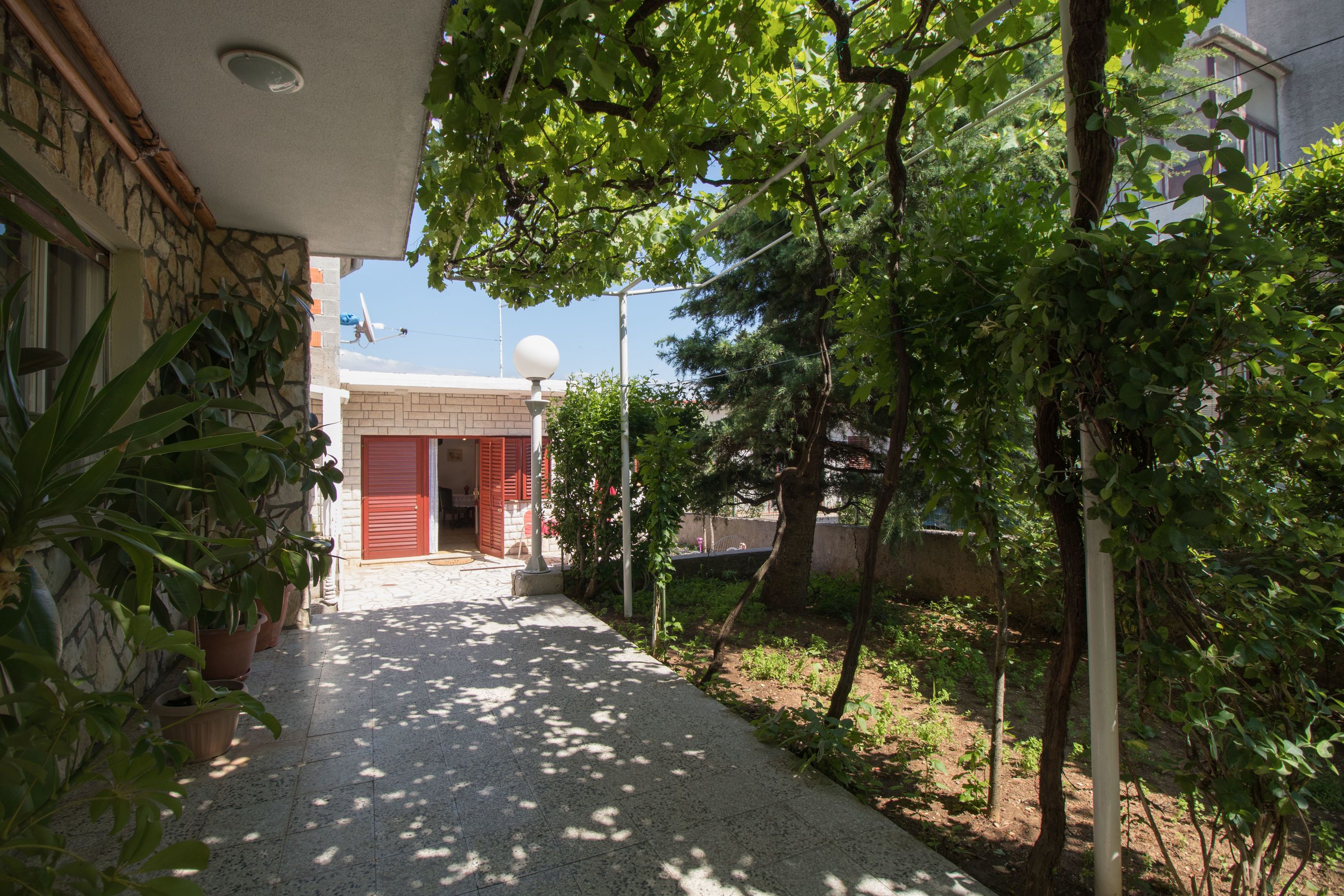 A courtyard with a paved walkway, potted plants, and a building with a red door.