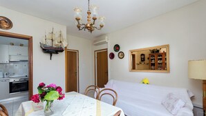 A room with a dining table, chairs, a bed, a chandelier, and a kitchen area. - Apartments Tugomila (Barbat)