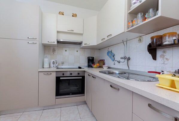 A kitchen with white cabinets, a stove, a sink, and a tiled backsplash.