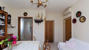 A dining area with a table set for two, a white sofa, and a wooden cabinet with decorative items. - Apartments Tugomila (Barbat)