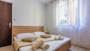 Una cama bien tendida con almohadas y toallas, un cabecero de madera, una lámpara de noche y una ventana con cortinas florales.