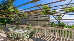 Un patio al aire libre con una mesa y sillas, una pérgola con plantas trepadoras y vista al mar.