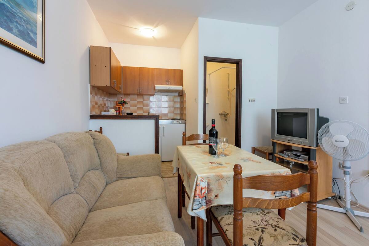 Ein kompakter Wohnbereich mit Sofa, Esstisch, Holzausbau, Fernseher und Ventilator.