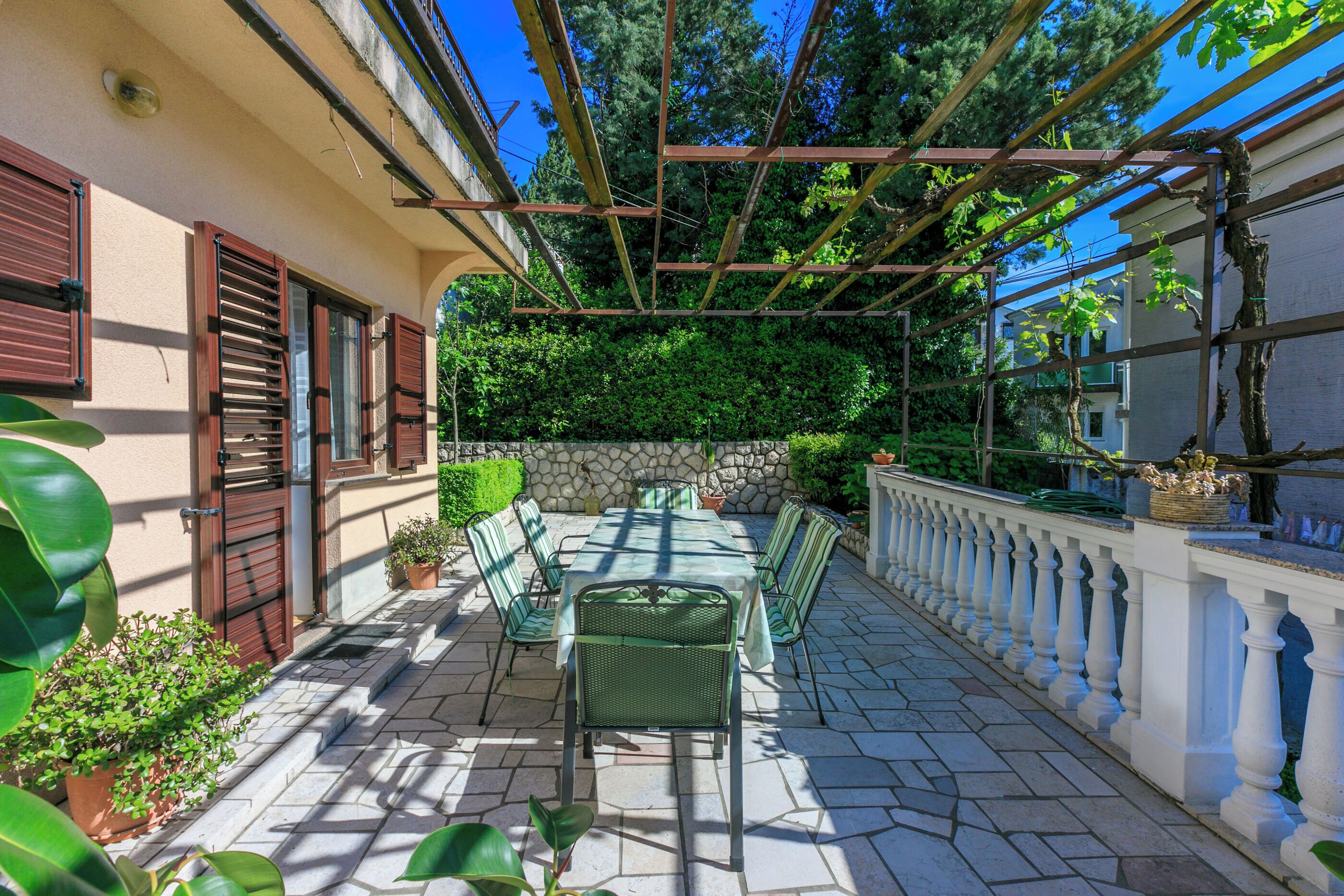 An outdoor patio with a table and chairs, surrounded by potted plants and a stone wall.