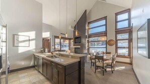 Una cocina moderna con una isla grande, armarios oscuros y un comedor con mesa y sillas.