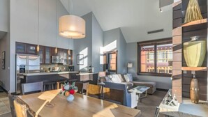 Amplia sala de estar con una mesa de comedor de madera, un conjunto de sofás y una cocina al fondo.