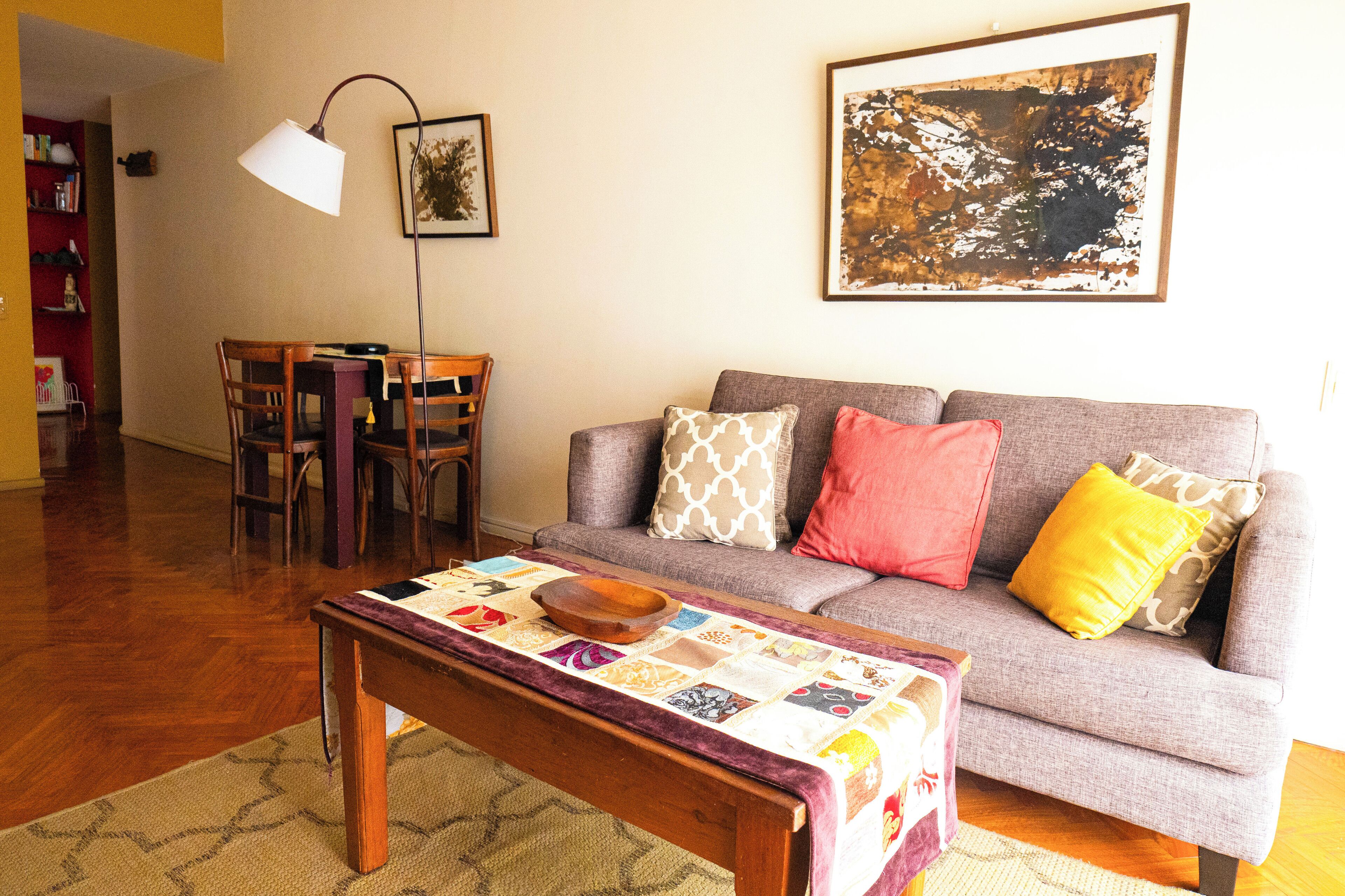 Uma sala de estar com sofá, mesa de centro, mesa de jantar com cadeiras e abajur.