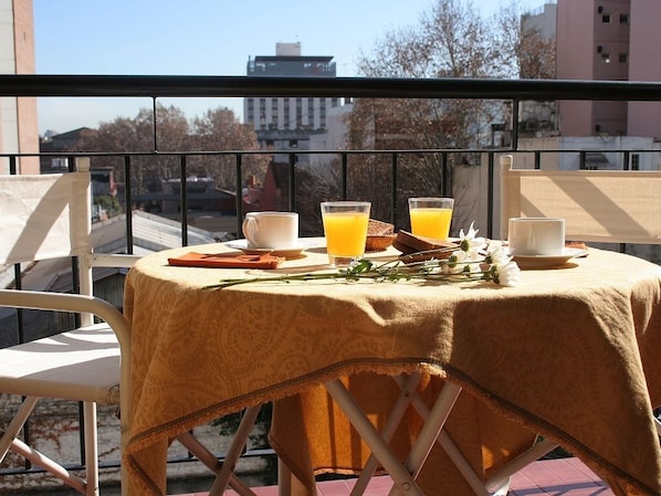 A balcony table with a tablecloth, two glasses of orange juice, a white mug, and a plate of food.