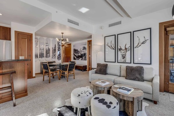 A spacious living area with a sofa, coffee table, and ottoman, a dining area with chairs and a table, and a kitchen with a refrigerator. - Capitol Peak Lodge 3222 (Snowmass)