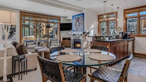 Een moderne woonkamer met een glazen eettafel, leren fauteuils, een open haard en grote ramen met uitzicht op de stad.