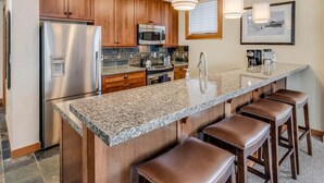 A kitchen with wooden cabinets, stainless steel appliances, granite countertops, and bar stools. - Capitol Peak Lodge 3210 (Snowmass Village)