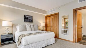 A bedroom with a large bed, two bedside tables with lamps, a wooden door, and a framed picture on the wall. - Capitol Peak Lodge 3210 (Snowmass Village)