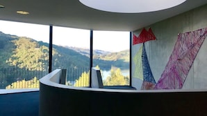 Habitació amb un finestral gran que ofereix vistes a un llac i muntanyes. Hi ha un lluminària moderna al sostre.