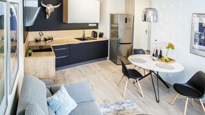 Una cocina moderna con encimera negra, electrodomésticos de acero inoxidable y una decoración con calavera de toro. Hay una zona de comedor con una mesa blanca y sillas negras.