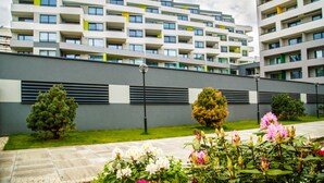 Un edificio de apartamentos moderno con varios balcones y un jardín bien cuidado con flores y arbustos.