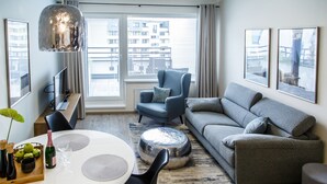 Una sala de estar moderna con sofá, sillón, mesa de comedor y un amplio ventanal con persianas.