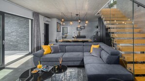 Una sala de estar moderna con un sofá seccional gris, una escalera de cristal y un comedor.