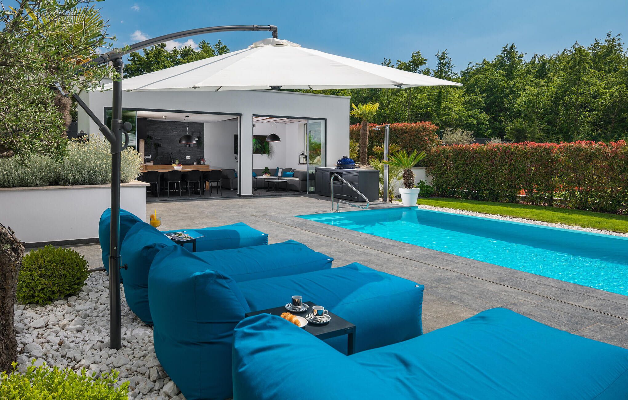 A modern outdoor pool area with blue seating, a covered patio, and a view of the pool.