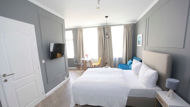 Habitación de hotel con cama, televisor montado en la pared, una mesita con sillas y una ventana con cortinas.