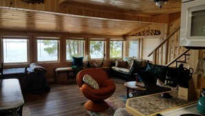 Acogedor interior de cabaña con paredes y suelos de madera, un sofá, una silla, una mesa y un televisor.