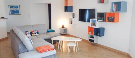 Una sala de estar moderna con un sofá gris, una mesa redonda blanca y un televisor montado en la pared.
