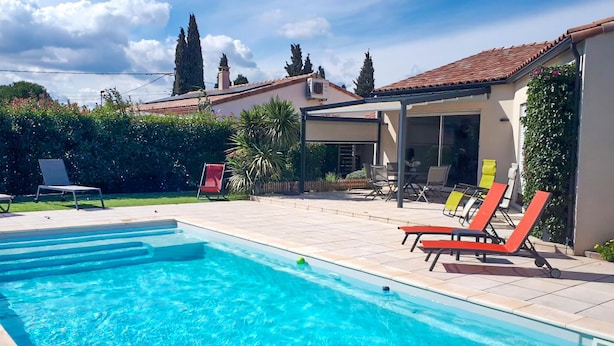 A swimming pool with clear blue water, surrounded by lounge chairs and a patio area with a covered seating section. - Cozy home in Ginestas with WiFi (Ginestas)