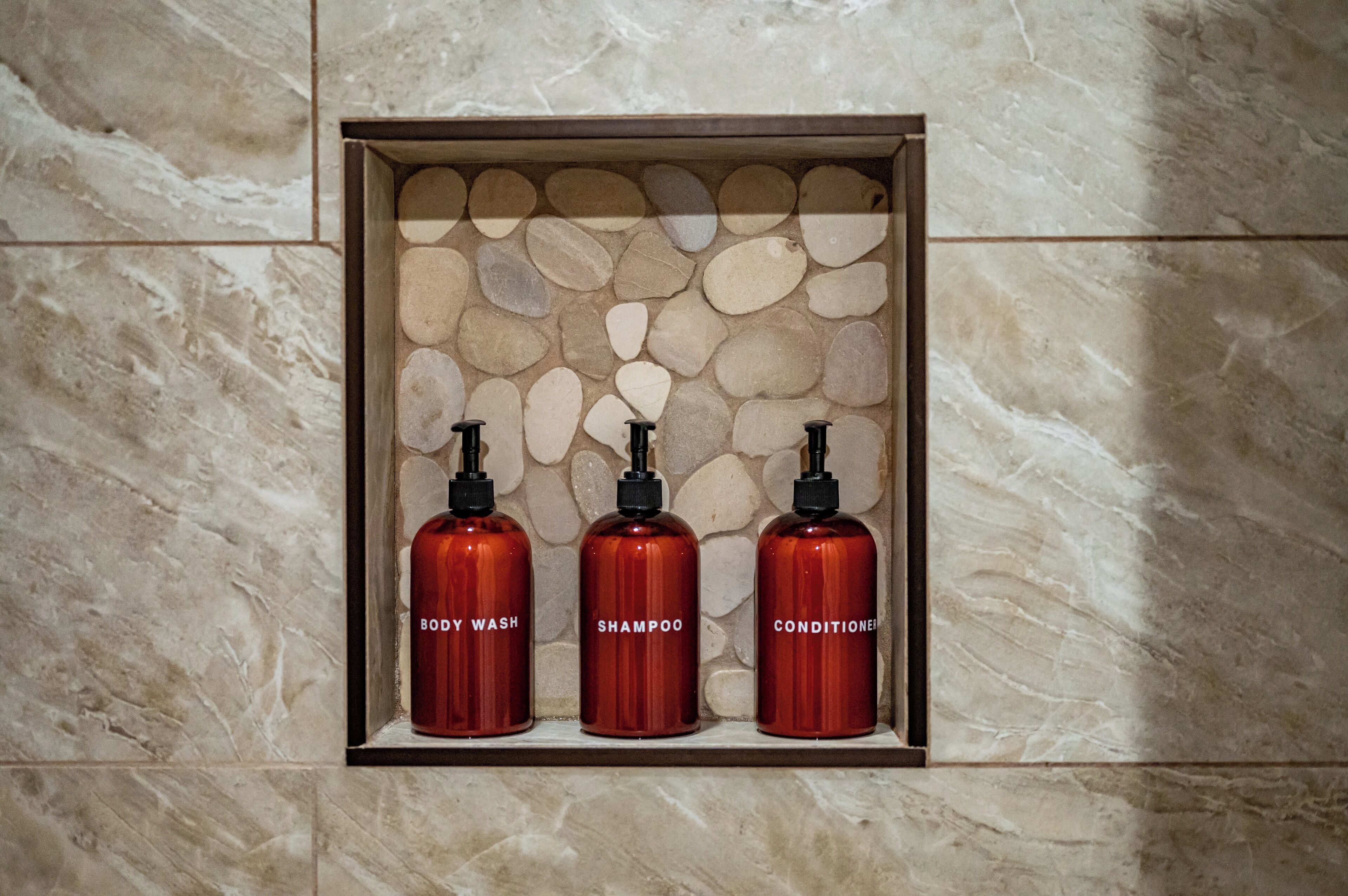Ein Badezimmer mit Marmorwand und einem Ablagefach mit drei Flaschen: Duschgel, Shampoo und Conditioner.