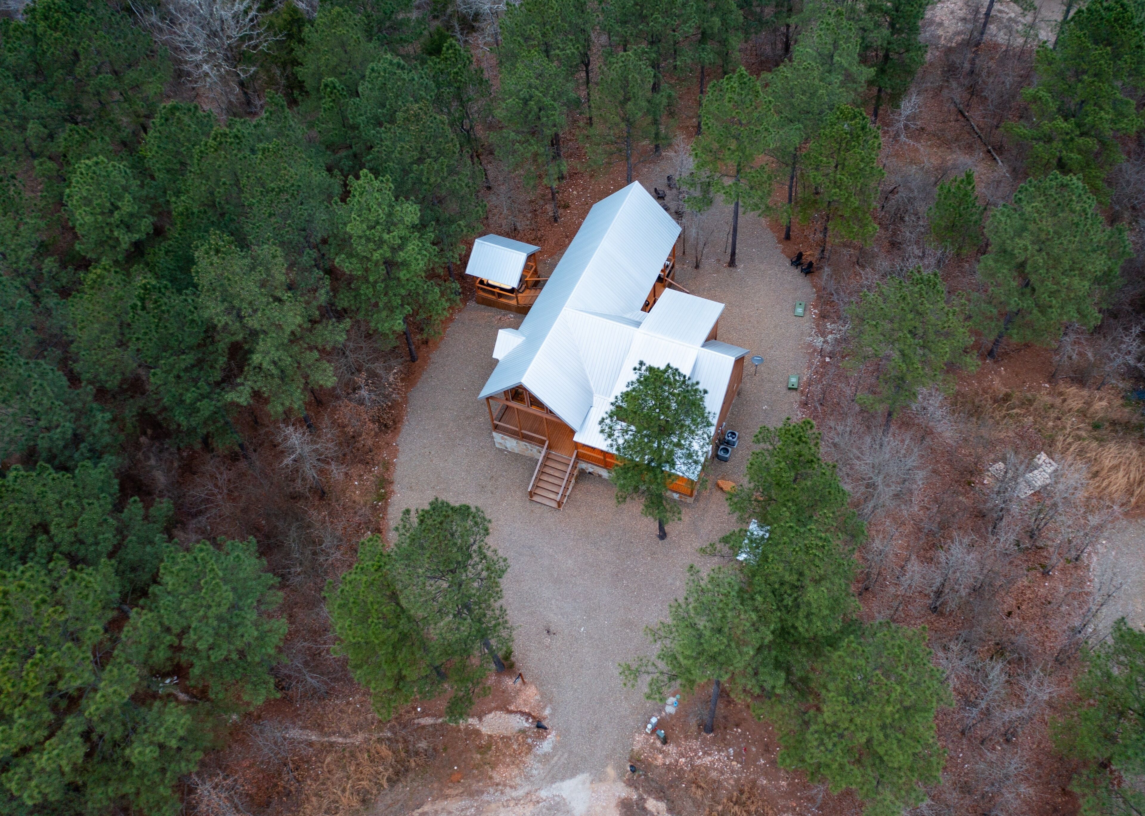 Vista aérea de una cabaña con un techo blanco grande, rodeada de un bosque denso.