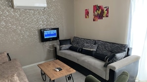 A living room with a grey sofa, a wooden coffee table, a TV mounted on the wall, and a wall-mounted air conditioner. - Celebi Apart Hotel (Izmir)