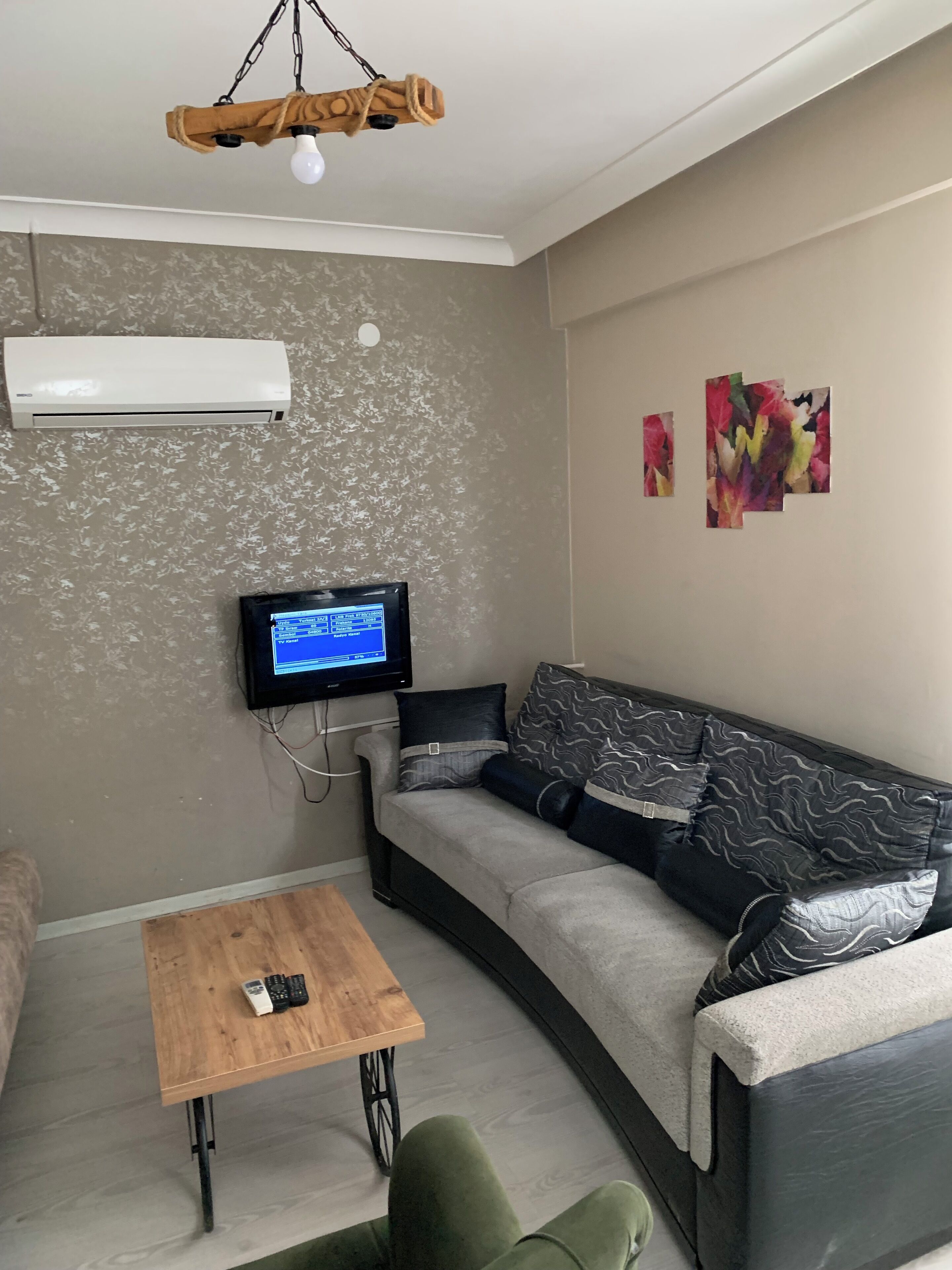 A living room with a sofa, a coffee table, a TV mounted on the wall, and an air conditioner.