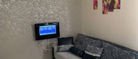 A living room with a sofa, a coffee table, a TV mounted on the wall, and an air conditioner.