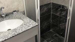 A bathroom with a granite countertop sink, a mirror, and a shower with a glass door. - Celebi Apart Hotel (Izmir)