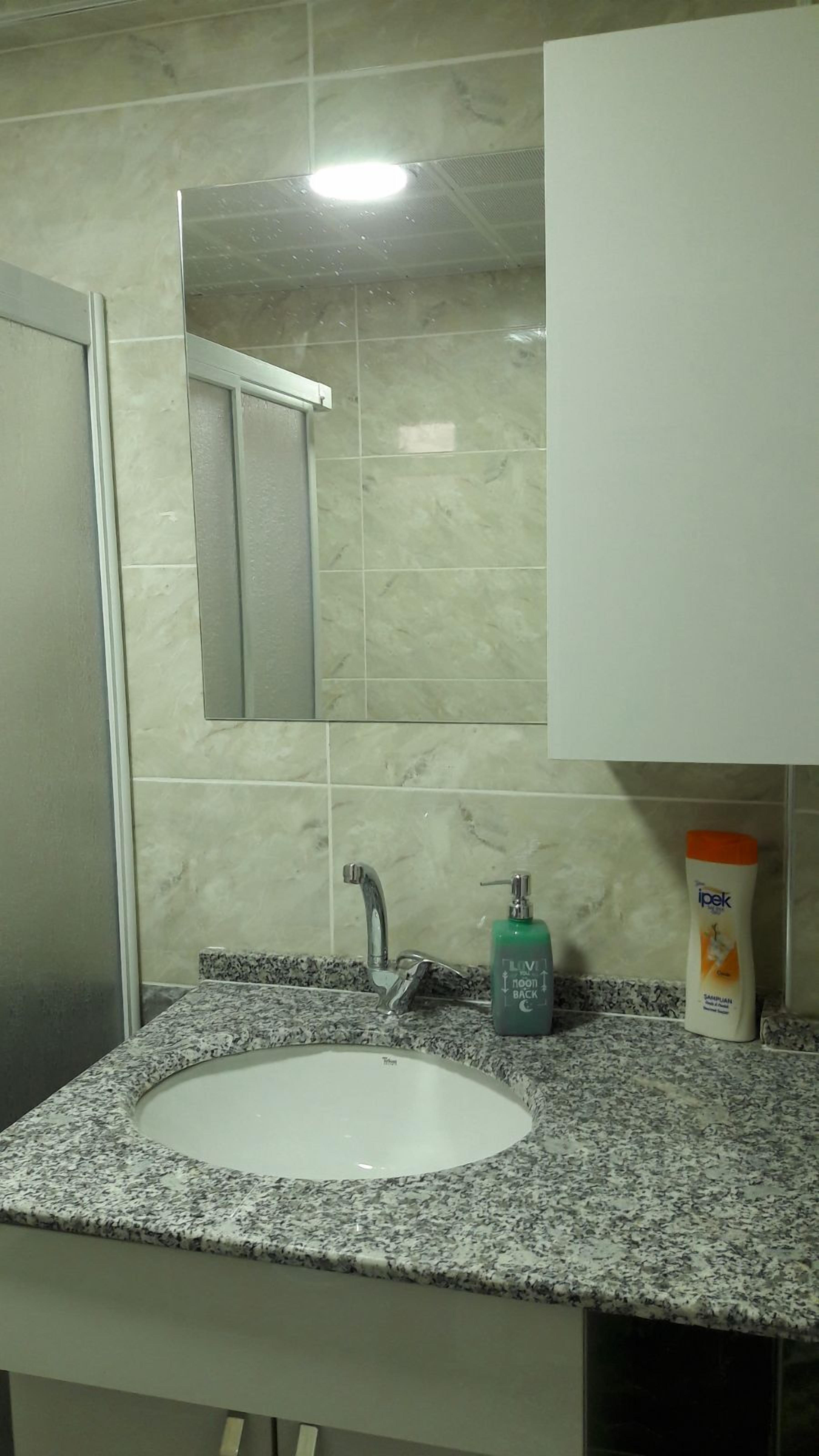 A bathroom with a granite countertop, a white sink, a mirror, and a soap dispenser.