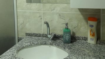 A bathroom with a granite countertop, a white sink, a mirror, and a soap dispenser.