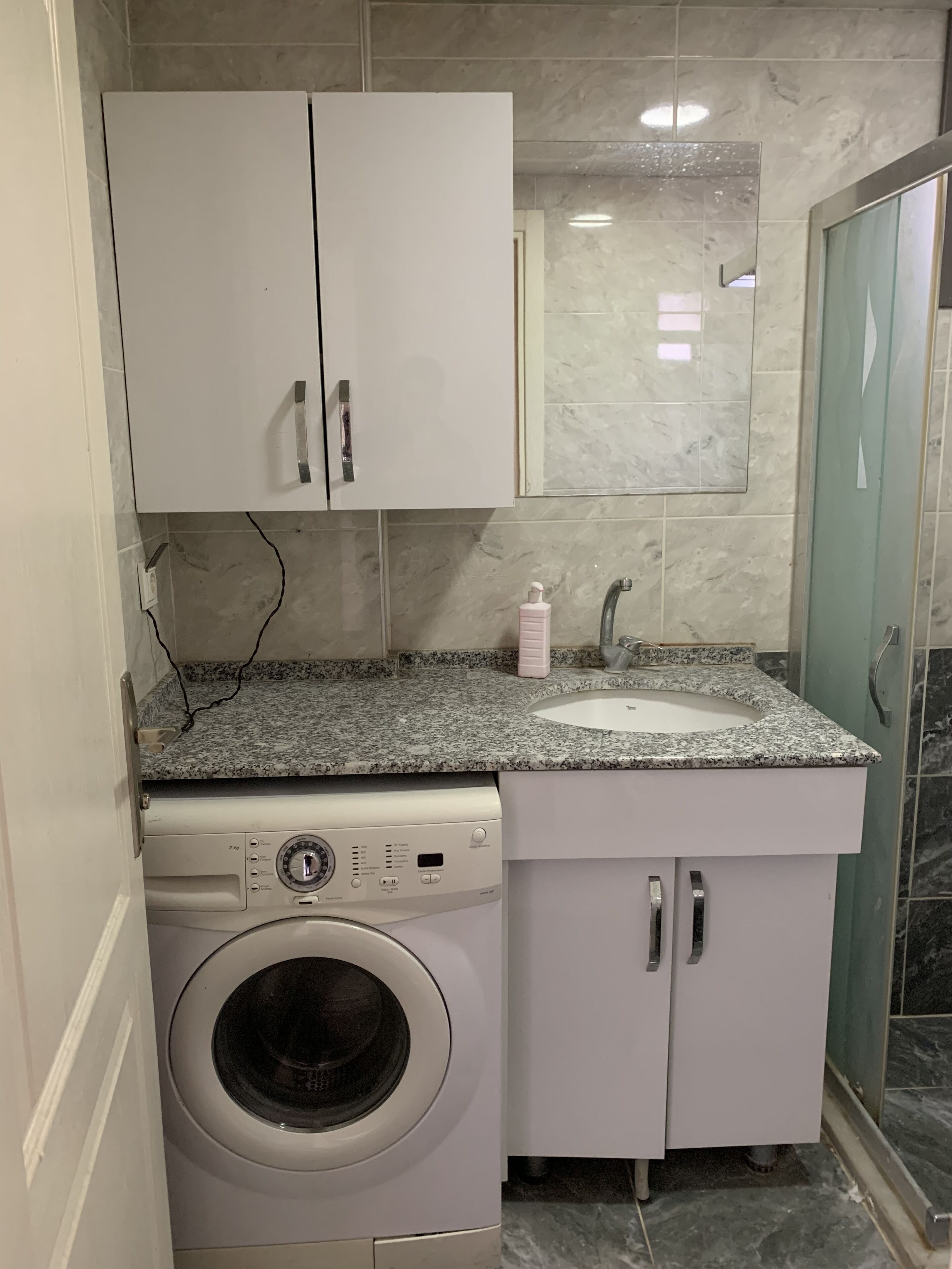 A compact bathroom with a washing machine, a sink, and a mirror.