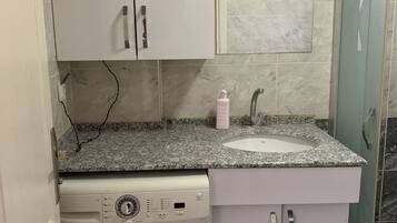 A compact bathroom with a washing machine, a sink, and a mirror.