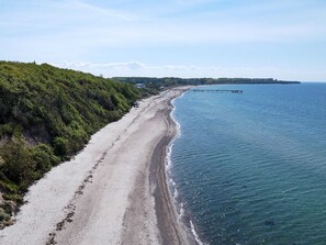 Eine Küstenstraße mit Strand, einem Steg und einem bewaldeten Hügel.