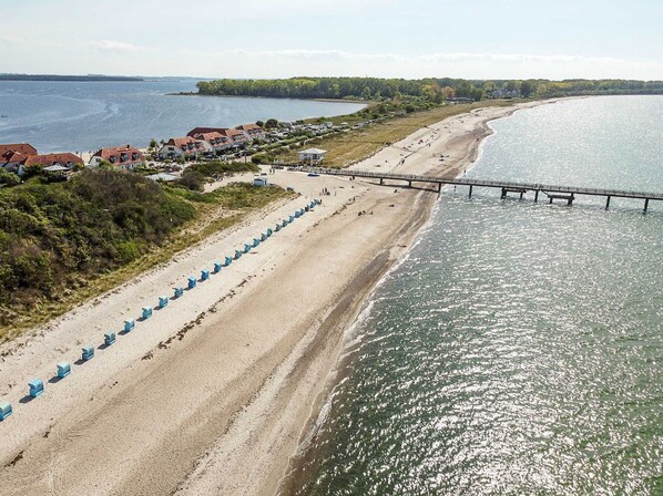 A beach with a pier, sandy shore, and a row of blue beach huts.