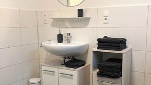 Un baño con lavamanos blanco, espejo y dos toalleros con toallas dobladas.