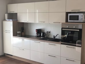 Et moderne køkken med hvide skabe, en mikrobølgeovn, kaffemaskine og ovn.