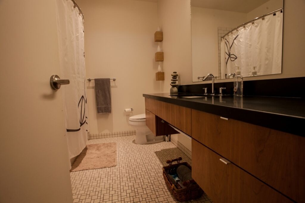 A bathroom with a tiled floor, a wooden vanity, a sink, a toilet, and a shower curtain.