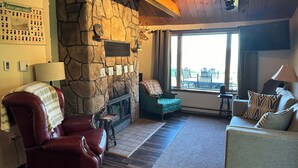 A cozy living room with a stone fireplace, leather armchair, and a view of the outdoors. - Freighters in front yard!  Private Sandy Beach - Large Deck - Best View on River (Sault Ste. Marie)