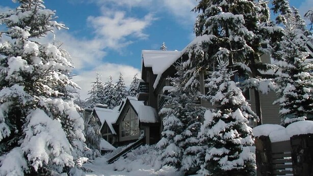 A snow-covered lodge with a steep roof, surrounded by snow-laden trees.