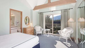 A bedroom with a bed, a dresser, a chair, a table, and a large window with curtains.
