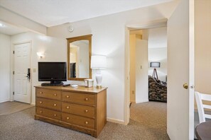 A hotel room with a wooden dresser, a television, a mirror, and a lamp.