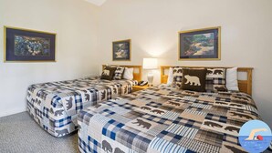 Una habitación con dos camas, cada una con colcha de cuadros con estampados de animales, una lámpara de noche y cuadros en las paredes.