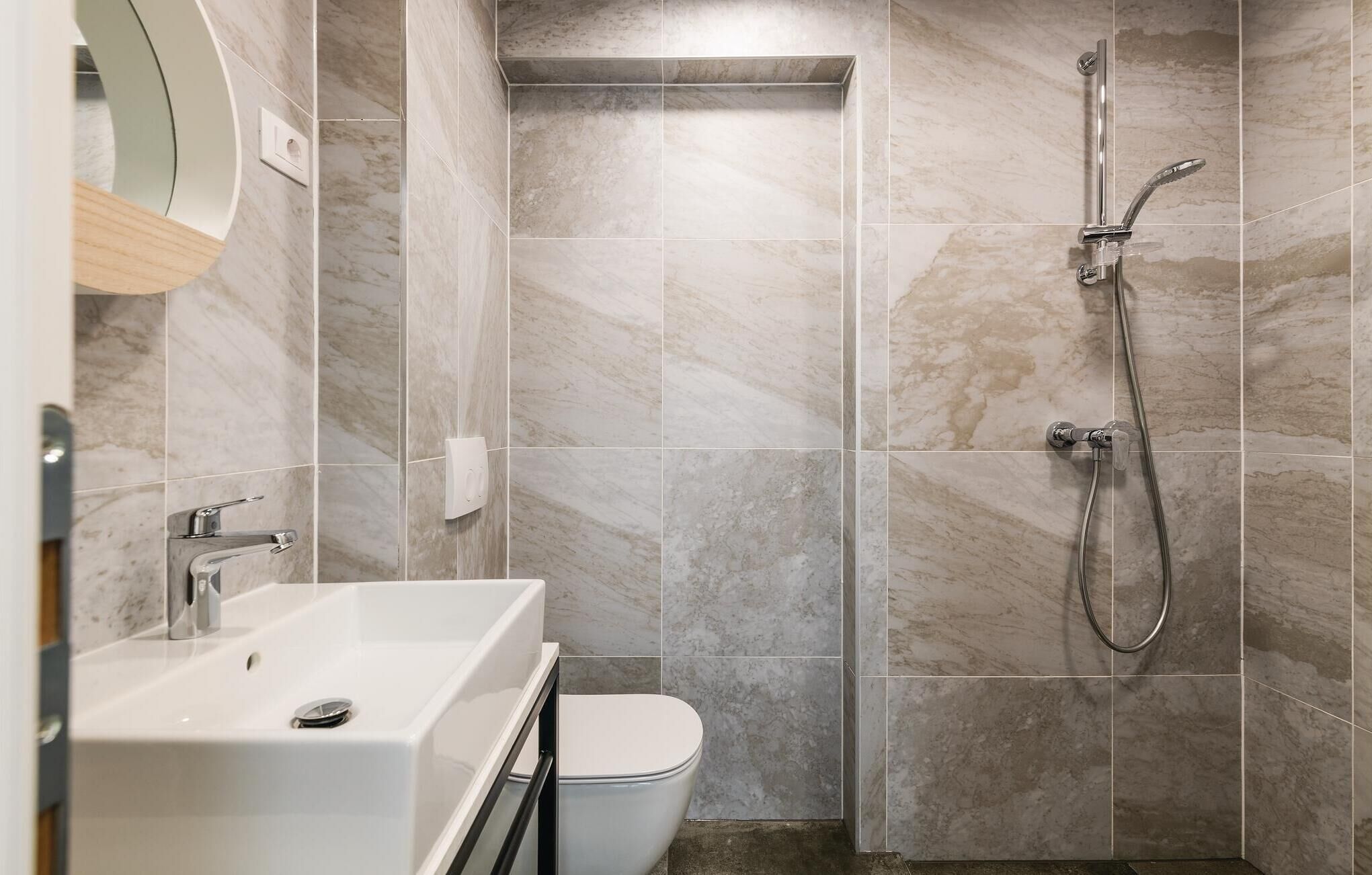 A modern bathroom with a white sink, a toilet, and a shower with a handheld showerhead.