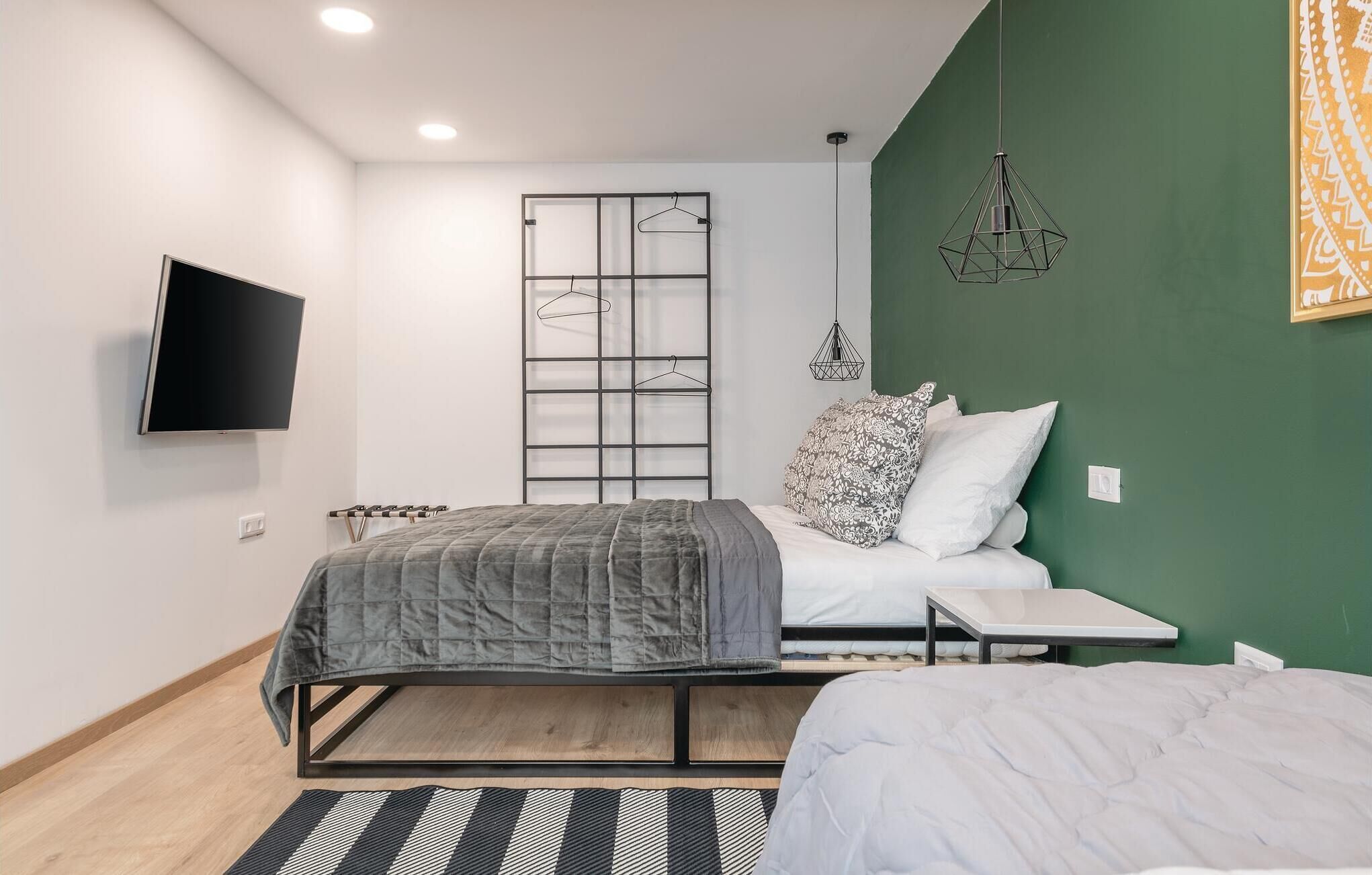 Une chambre avec un lit, une télévision, une lampe suspendue et un mur d’accent de couleur verte.